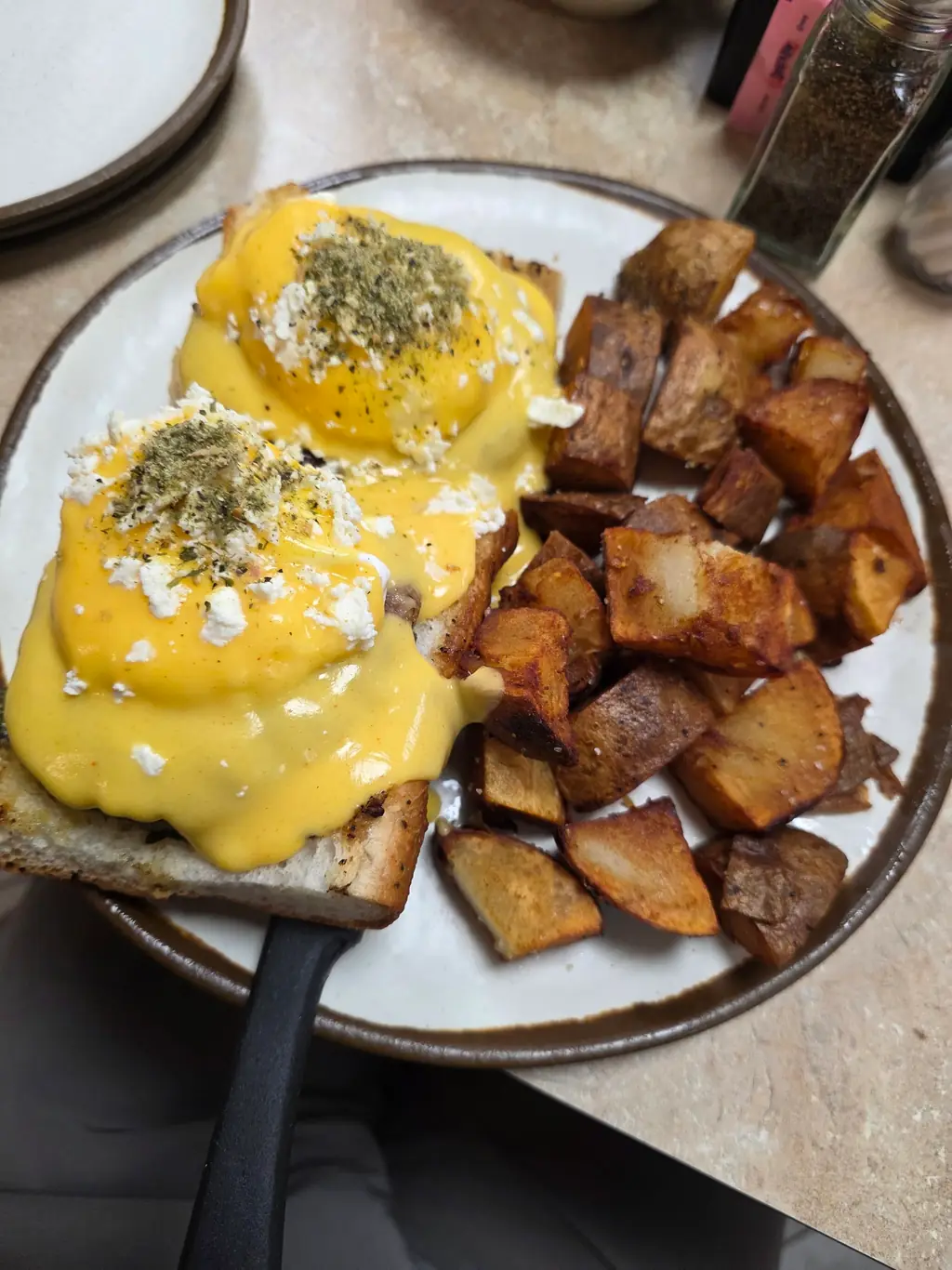 A Greek-style benedict with feta, hollandaise and herbs on toast beside home fries at 43rd Street Deli